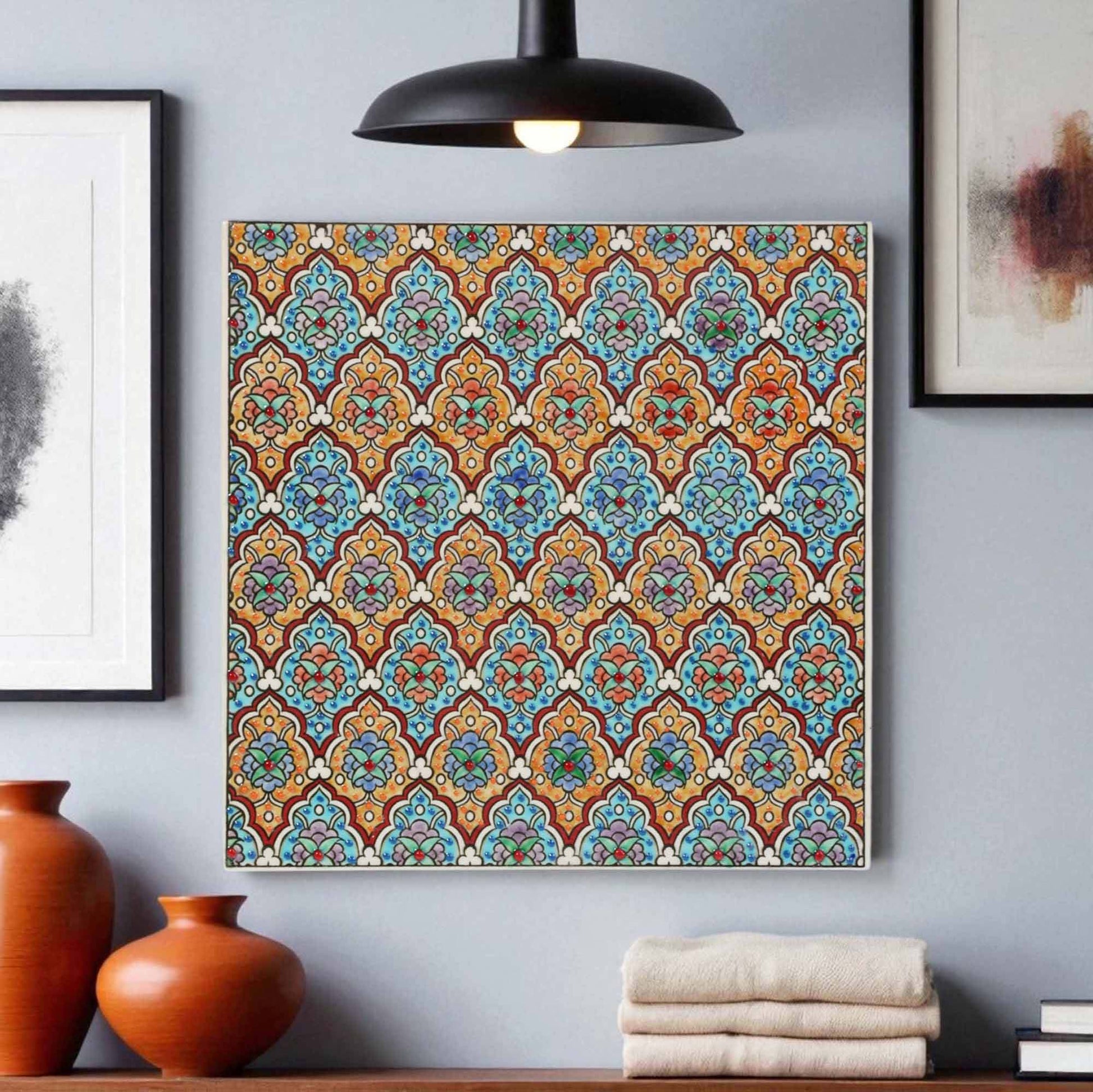 Decorative ceramic tile wall art with a colorful pattern on a gray wall, surrounded by vases and books.