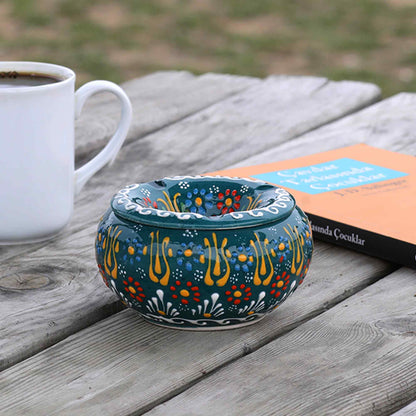 Decorative ceramic ashtray with floral patterns on a wooden table with a cup of coffee and book.