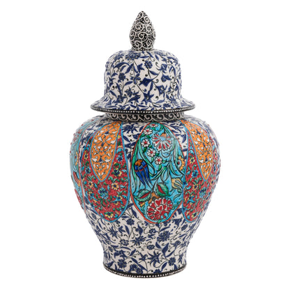 A hand-painted ceramic jar with a lid, featuring colorful floral patterns and bird motifs on a blue-and-white botanical base, with a decorative finial on the lid.