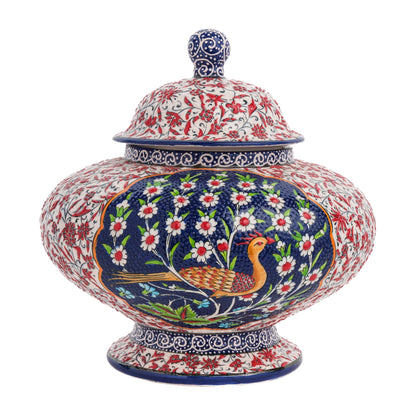 A hand-painted ceramic jar with a lid, featuring a bird amidst white flowers on a rich blue background, with additional floral motifs in vibrant colors.
