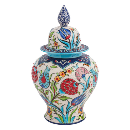 A hand-painted ceramic jar with a floral festival design, featuring red carnations, blue tulips, and yellow blossoms, and a blue ornate lid with a cobalt finial.