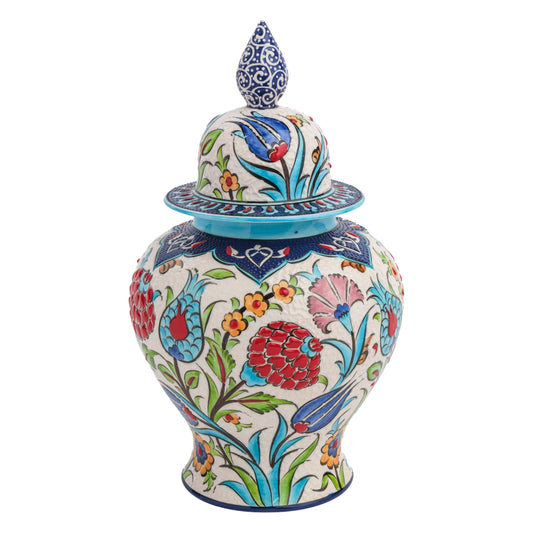 A hand-painted ceramic jar with a floral festival design, featuring red carnations, blue tulips, and yellow blossoms, and a blue ornate lid with a cobalt finial.