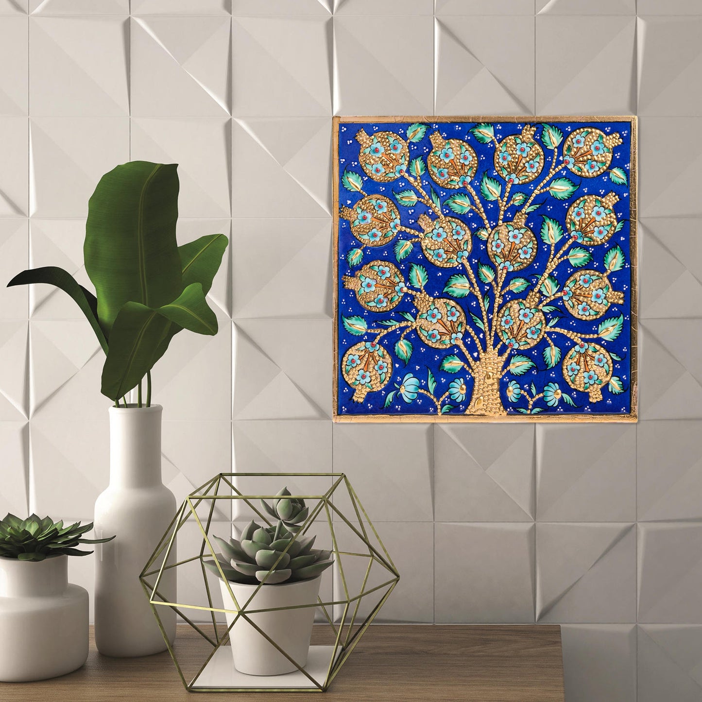 Decorative tree of life ceramic tile on a blue background next to potted plants.