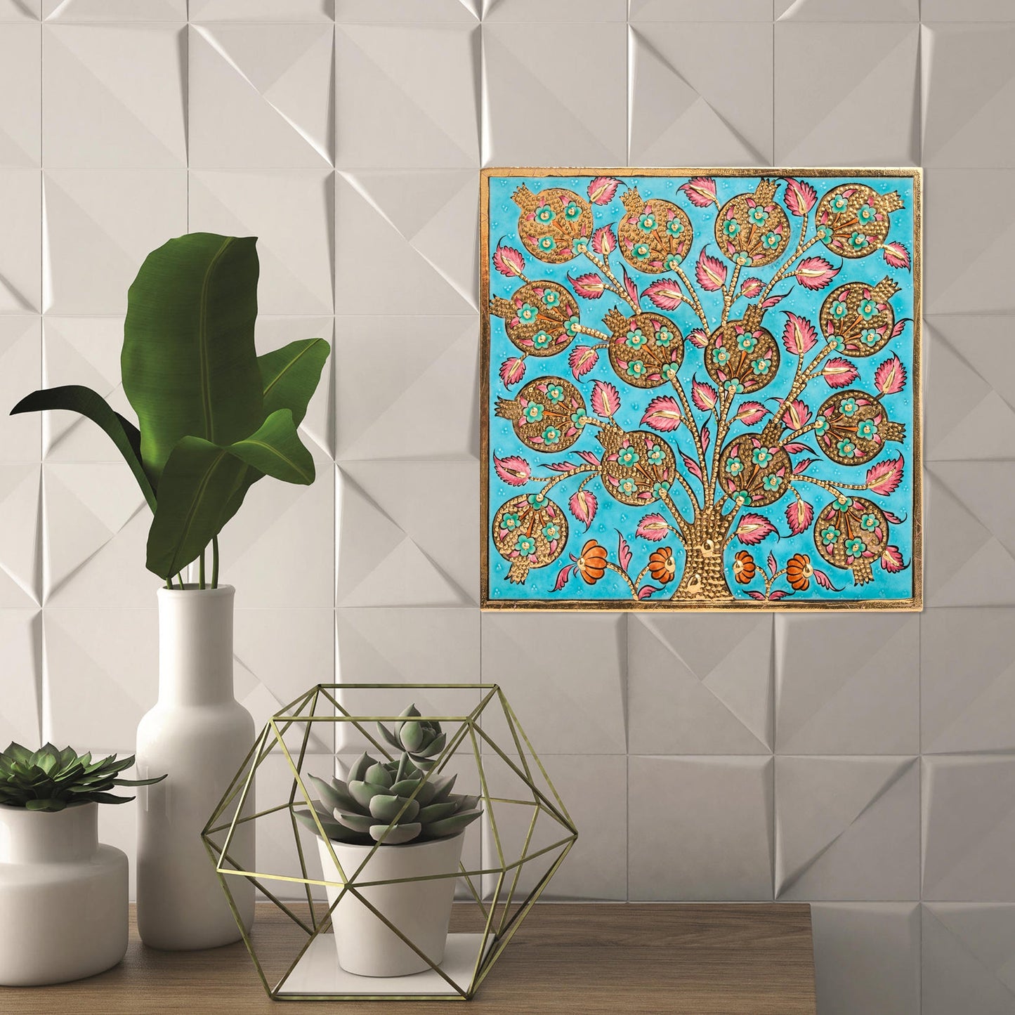 Decorative ceramic tile with floral tree design on a blue background, next to potted plants and a vase.