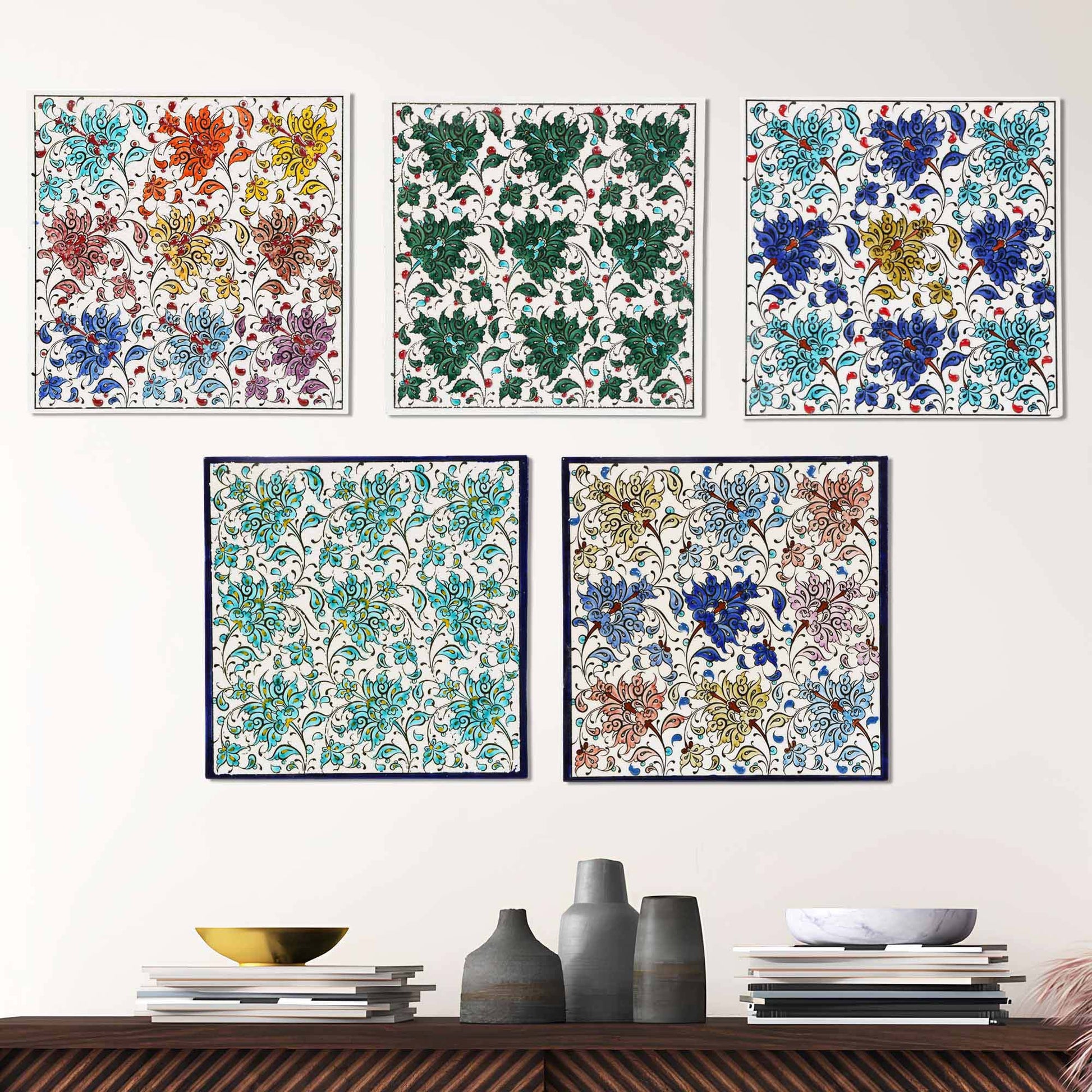 Set of five floral patterned ceramic tile pieces on a white wall above a wooden shelf with decorative items.