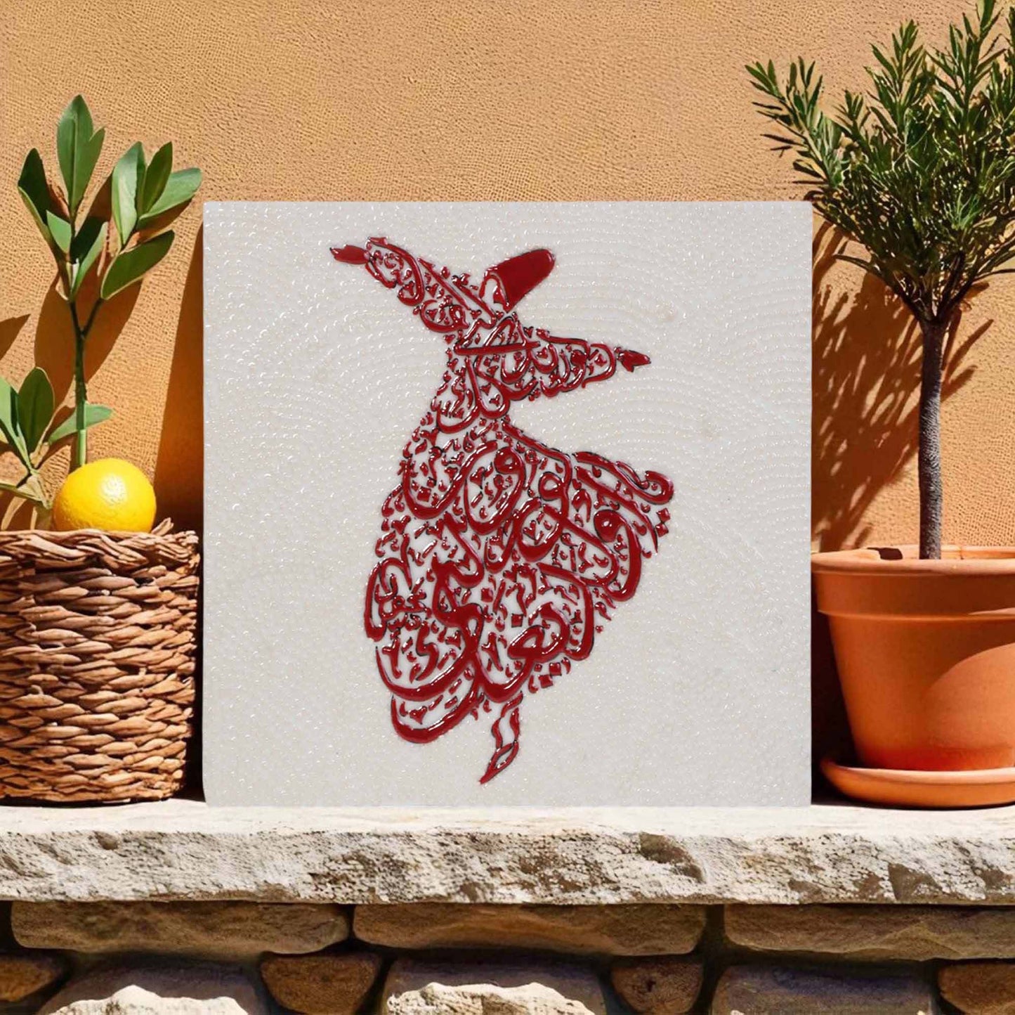 Decorative wall tile with a red Arabic calligraphy design on a white background, placed on a stone ledge with plants.