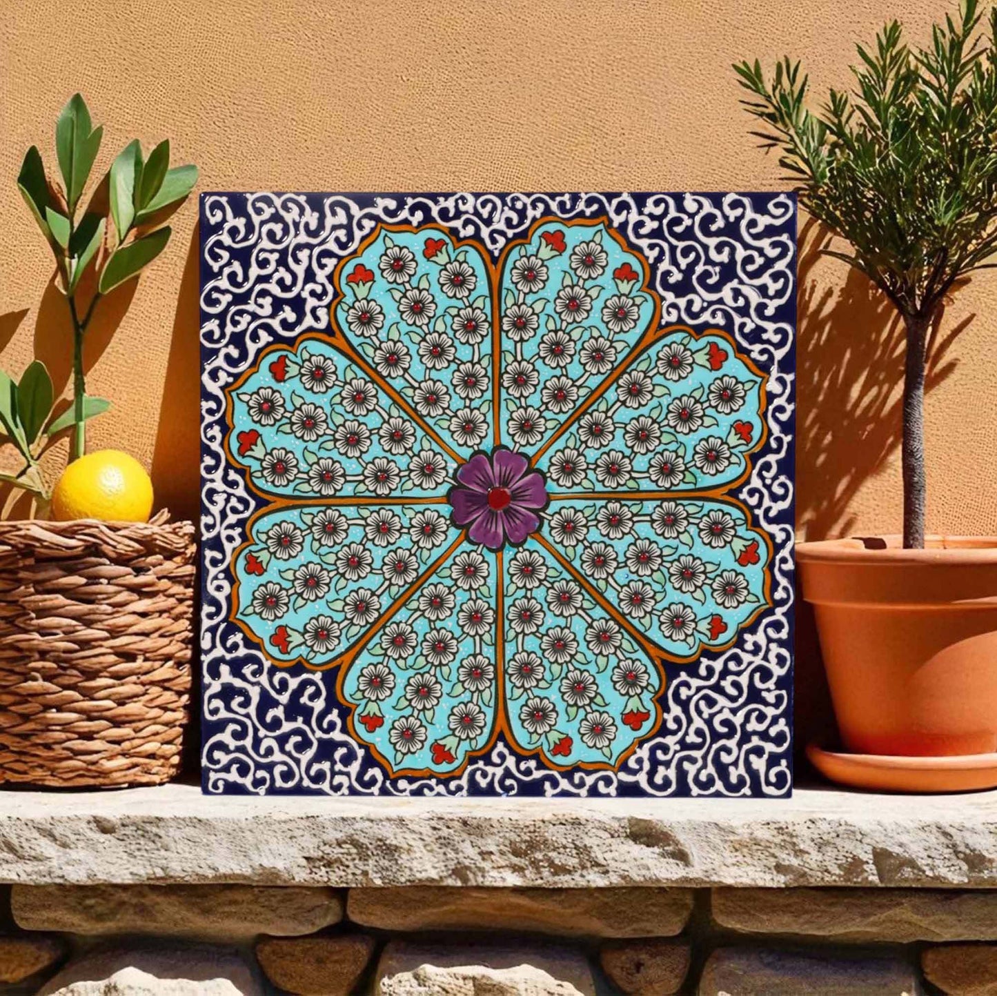 Decorative ceramic tile with a floral pattern on a stone ledge with plants.