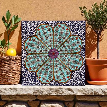 Decorative ceramic tile with a floral pattern on a stone ledge with plants.