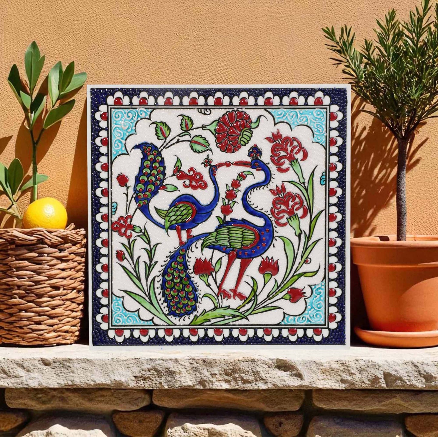 Decorative ceramic tile with peacock design on a stone ledge with plants