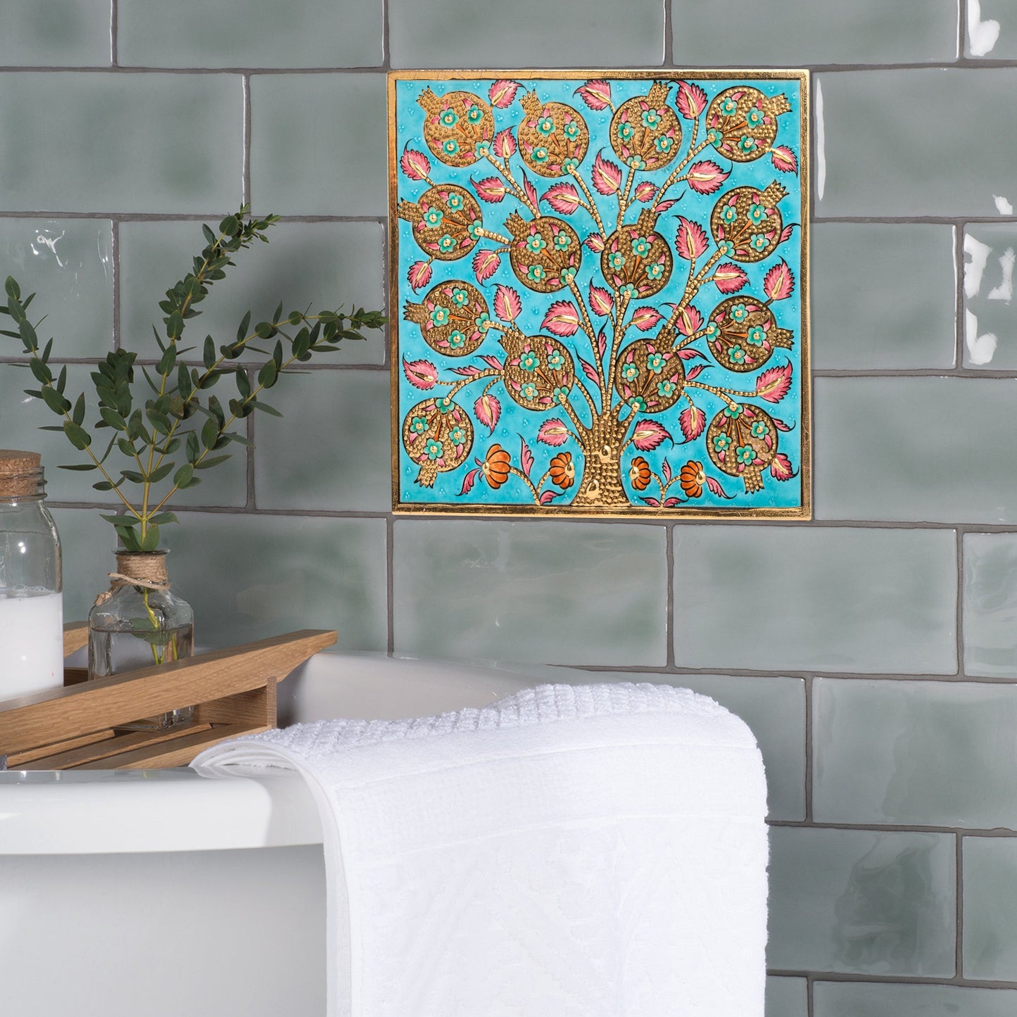 Decorative ceramic tile of a tree with colorful patterns on a turquoise background, hanging on a tiled wall above a sink.