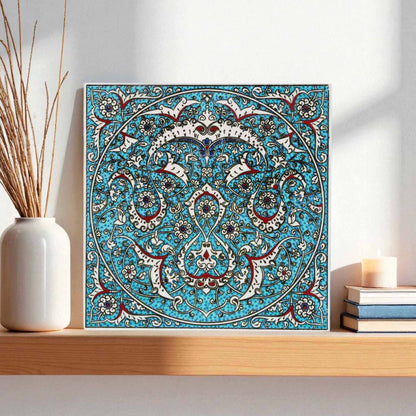 Decorative ceramic tile with intricate blue and white pattern on a shelf with a vase and books.