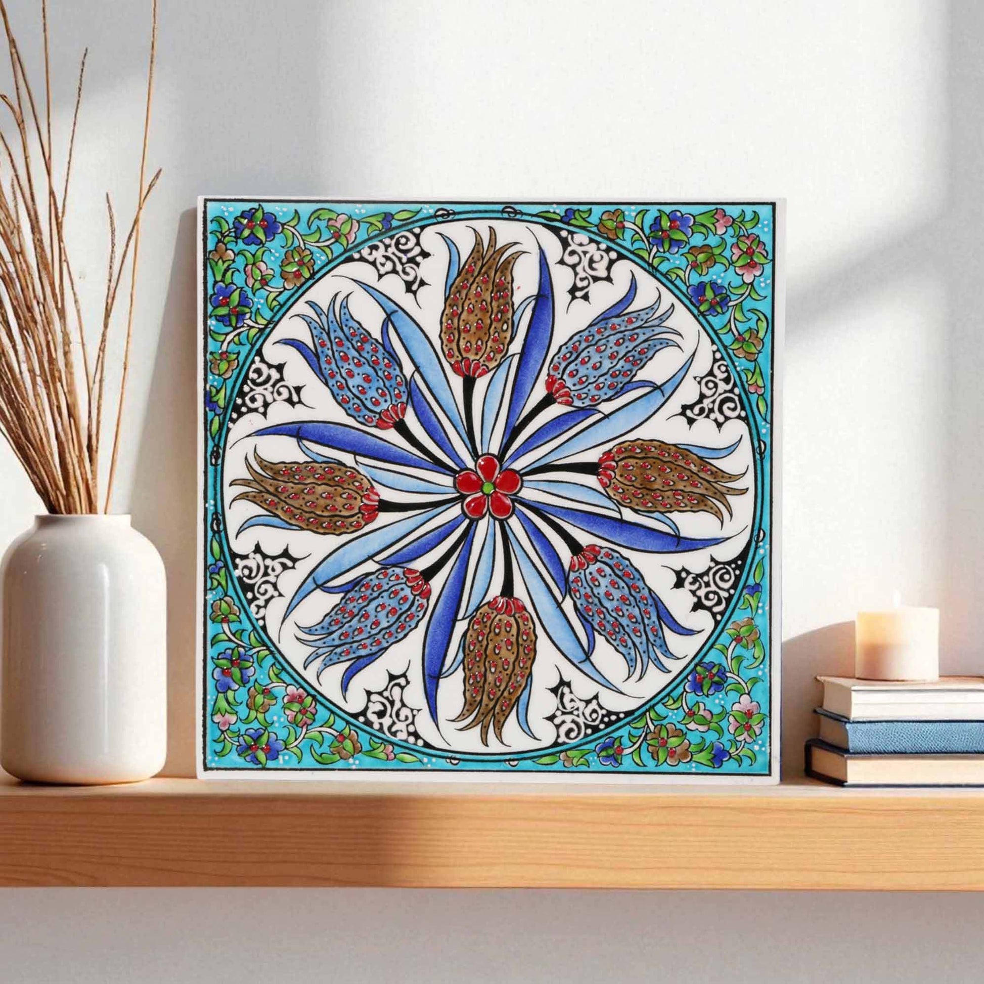 Decorative ceramic tile with floral pattern on a shelf with books and a candle