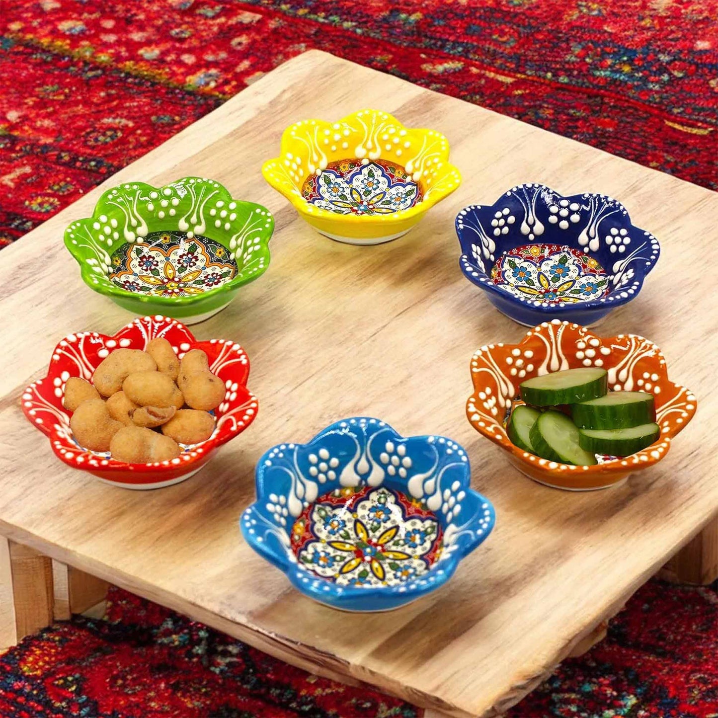 Colorful ceramic dip bowls on a wooden table with a patterned rug background