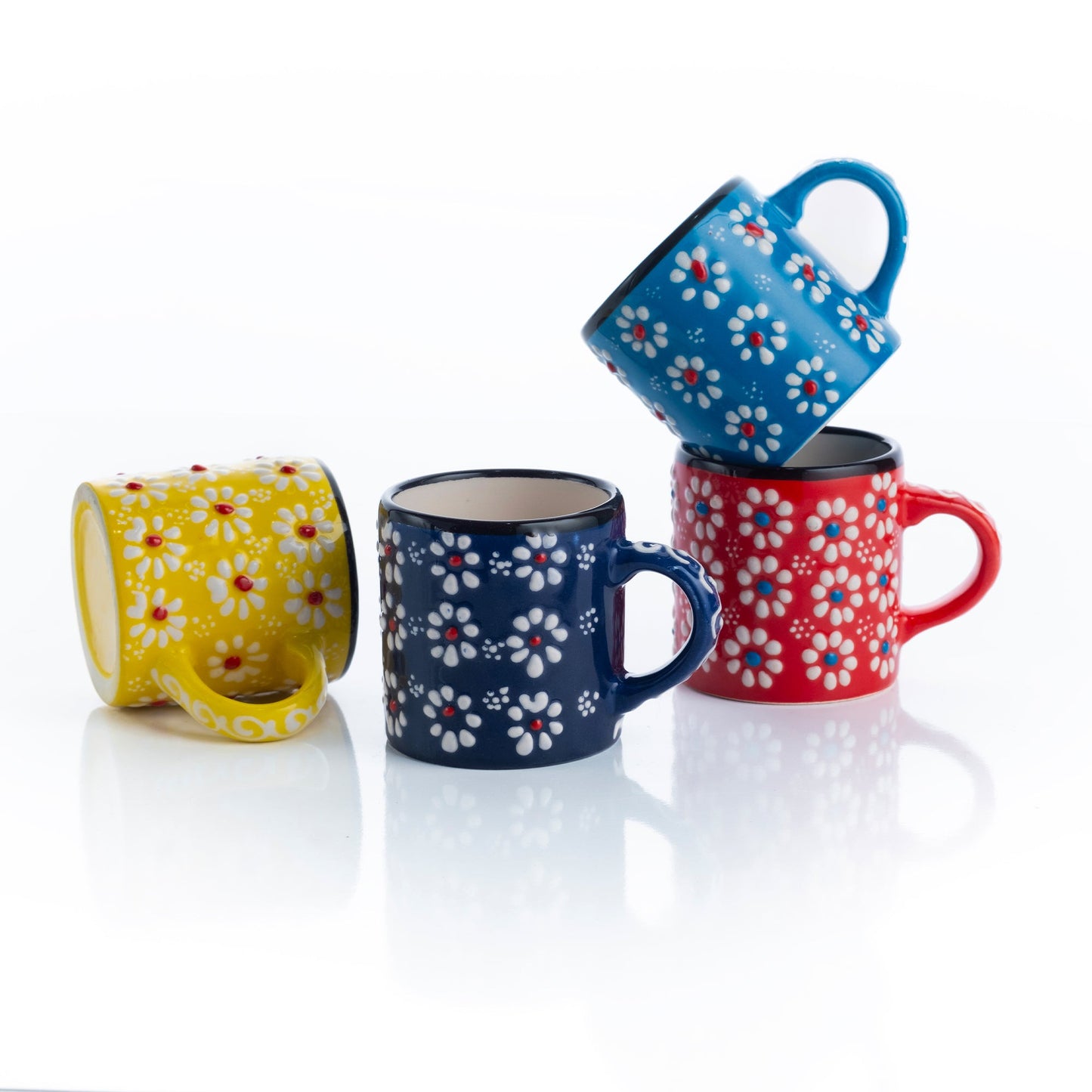 A set of four ceramic espresso cups in red, blue, yellow, and multicolored patterns, each cup with a handle and floral designs.