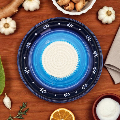 Blue ceramic garlic grater bowl with white center on a wooden surface with decorative items.