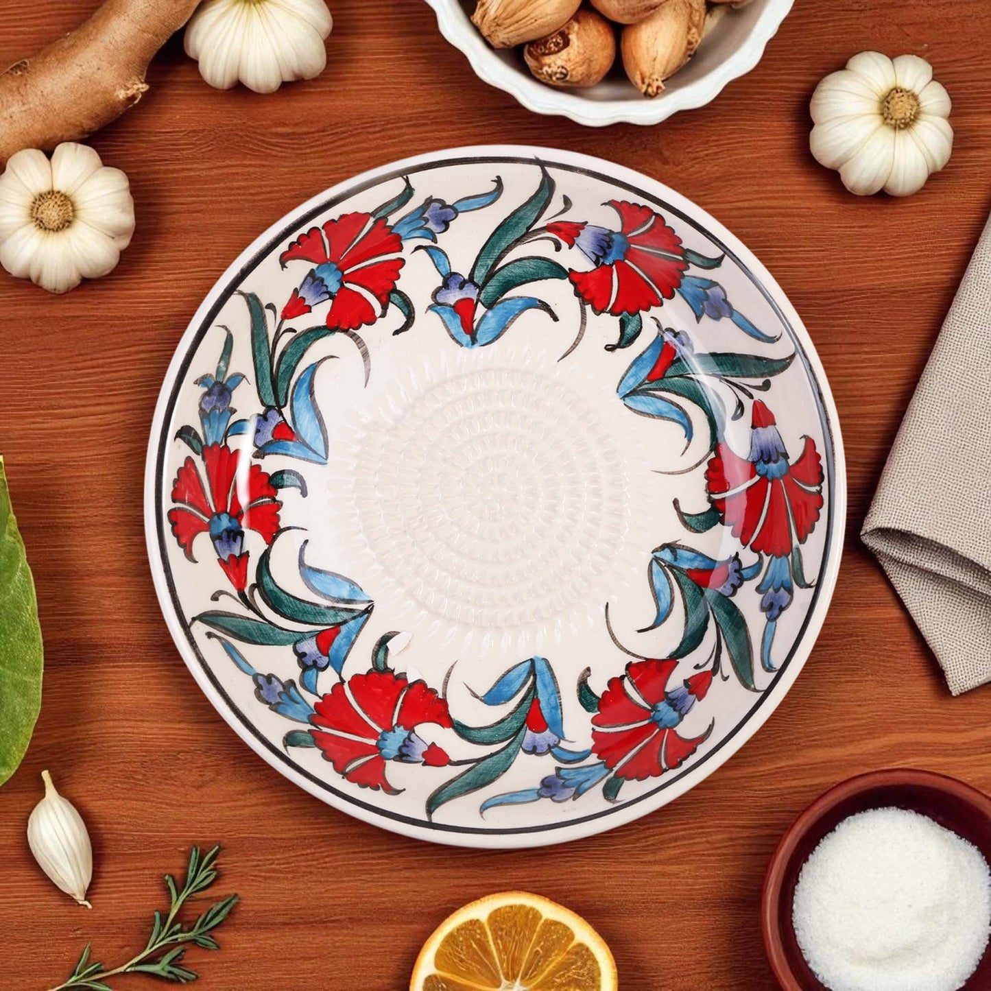 Decorative garlic grater bowl with floral design on a wooden table with ingredients