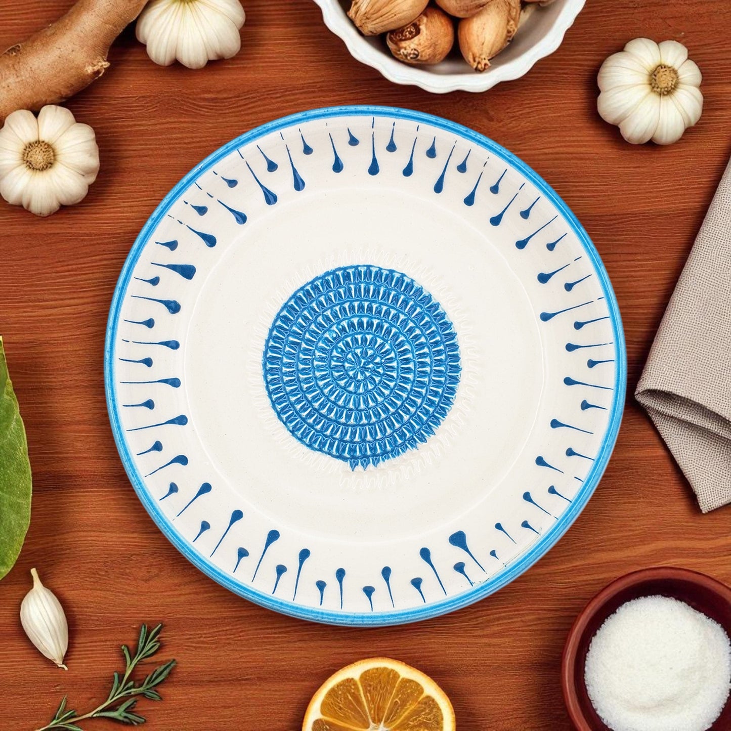 Ceramic garlic grater bowl with blue and white design on a wooden surface with decorative items.
