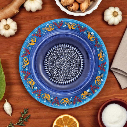 Decorative blue garlic grater bowl with floral patterns on a wooden table with ingredients.