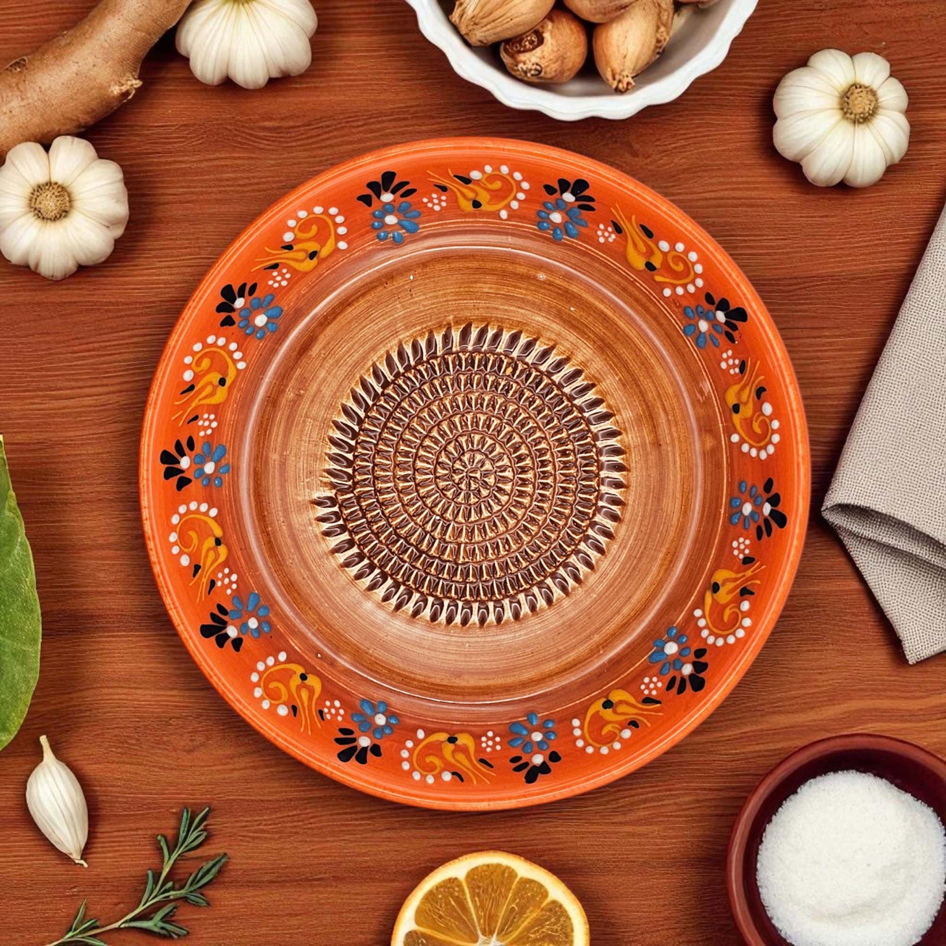 Decorative ceramic garlic grater bowl with floral patterns on a wooden surface with ingredients.