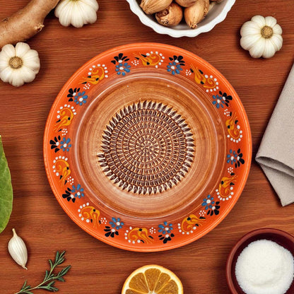 Decorative ceramic garlic grater bowl with floral patterns on a wooden surface with ingredients.