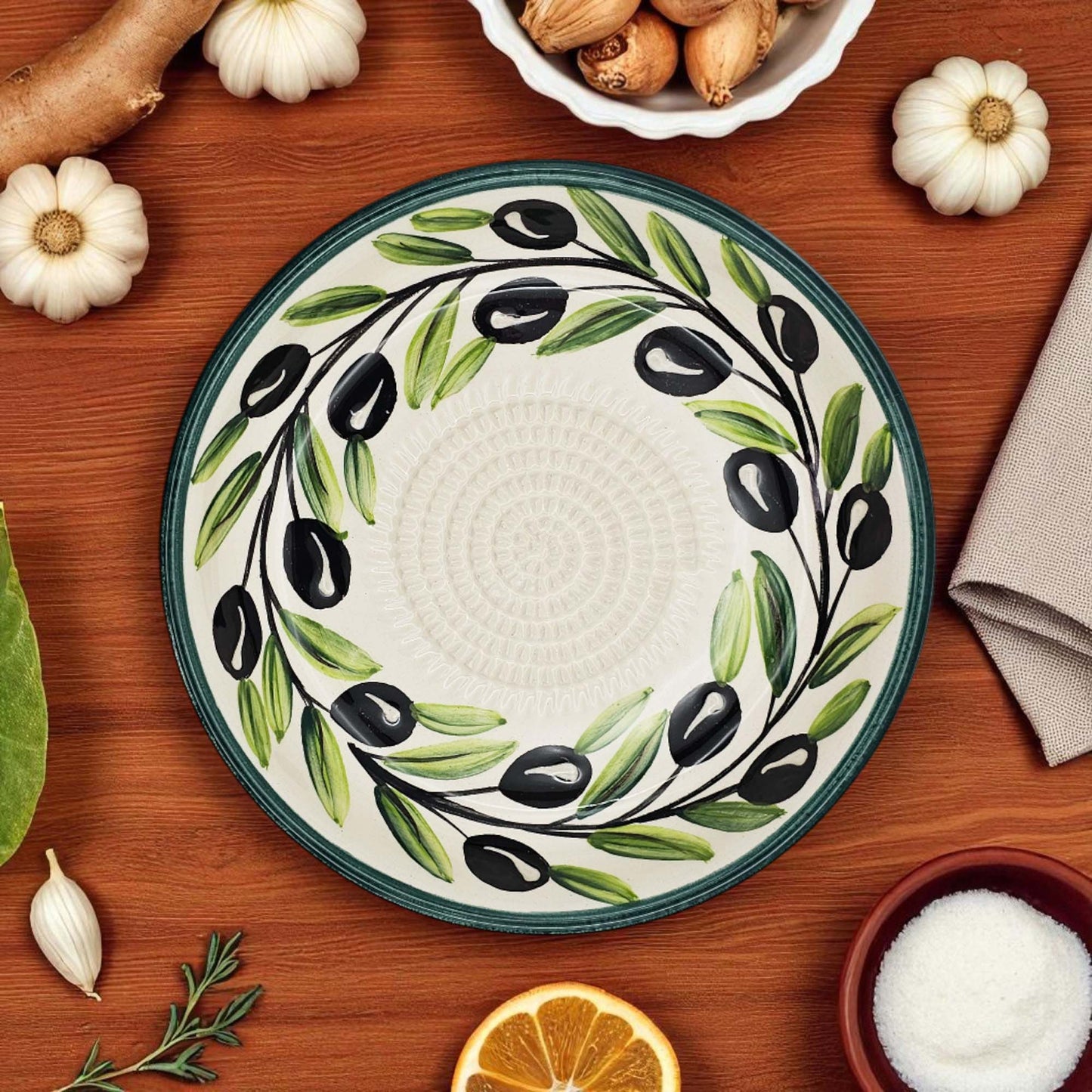 Decorative ceramic garlic grater bowl with olive design on a wooden table with ingredients.