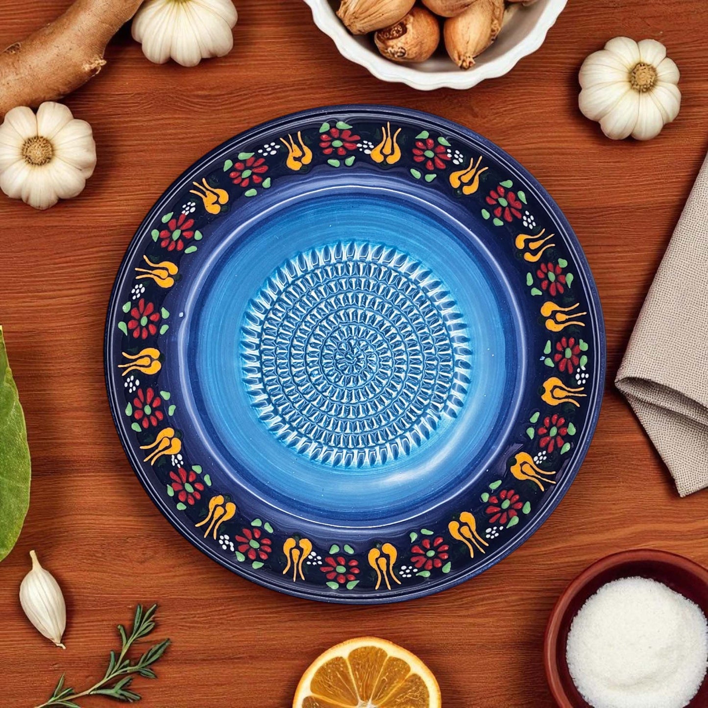Decorative blue garlic grater bowl with floral patterns on a wooden surface with ingredients.