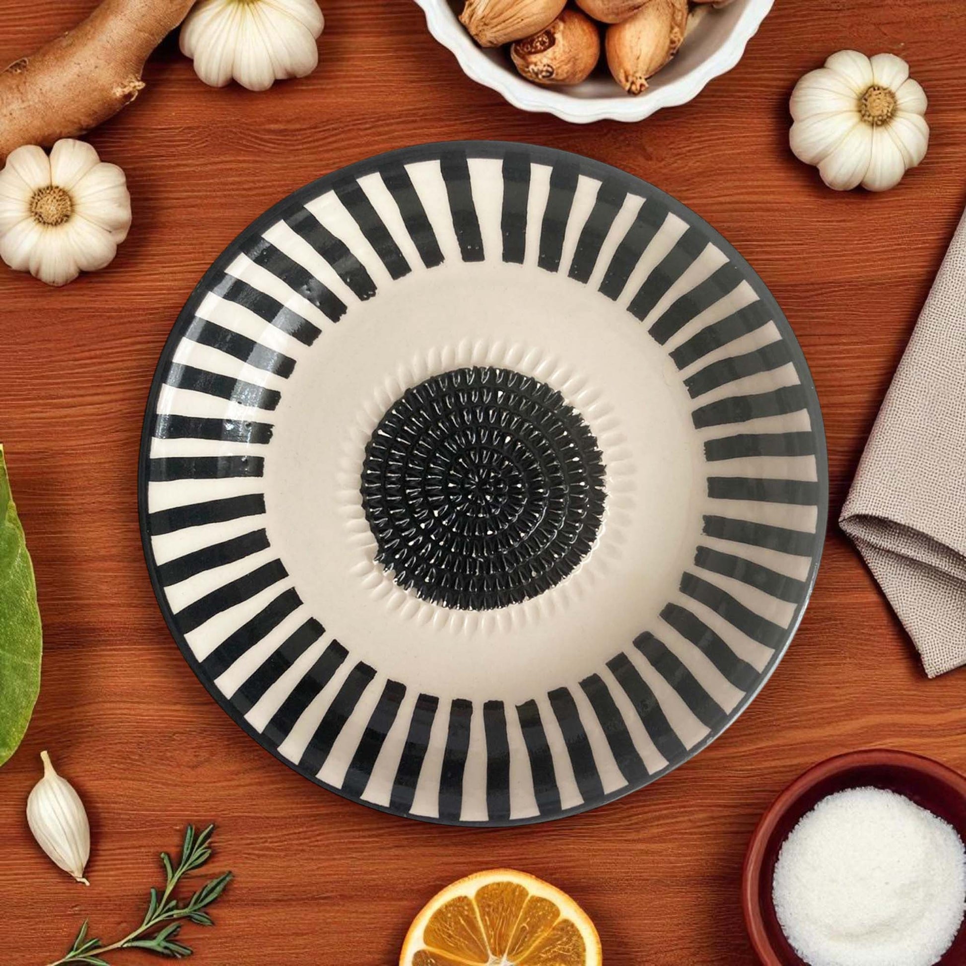 Decorative garlic grater bowl with black and white striped design on a wooden surface with pumpkins and other items.