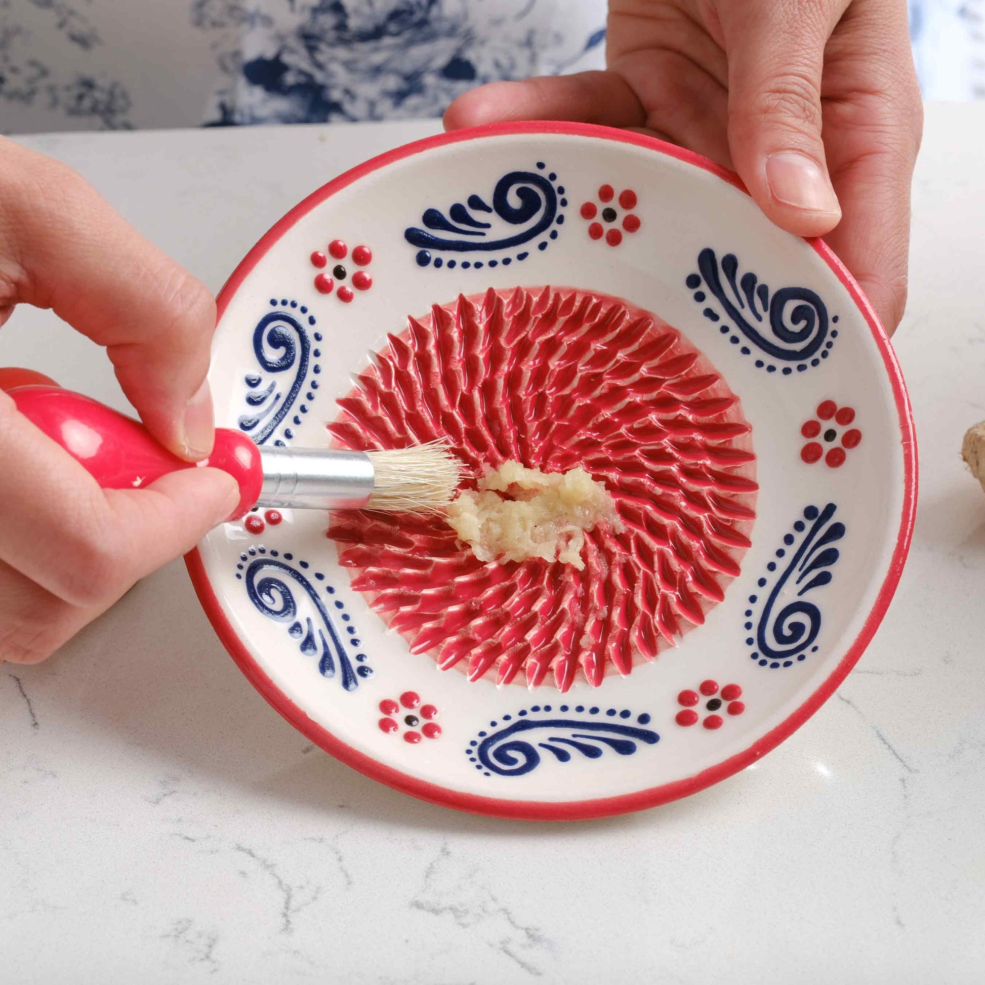 Person applying a paste to a decorative ceramic garlic grater plates with red and blue patterns