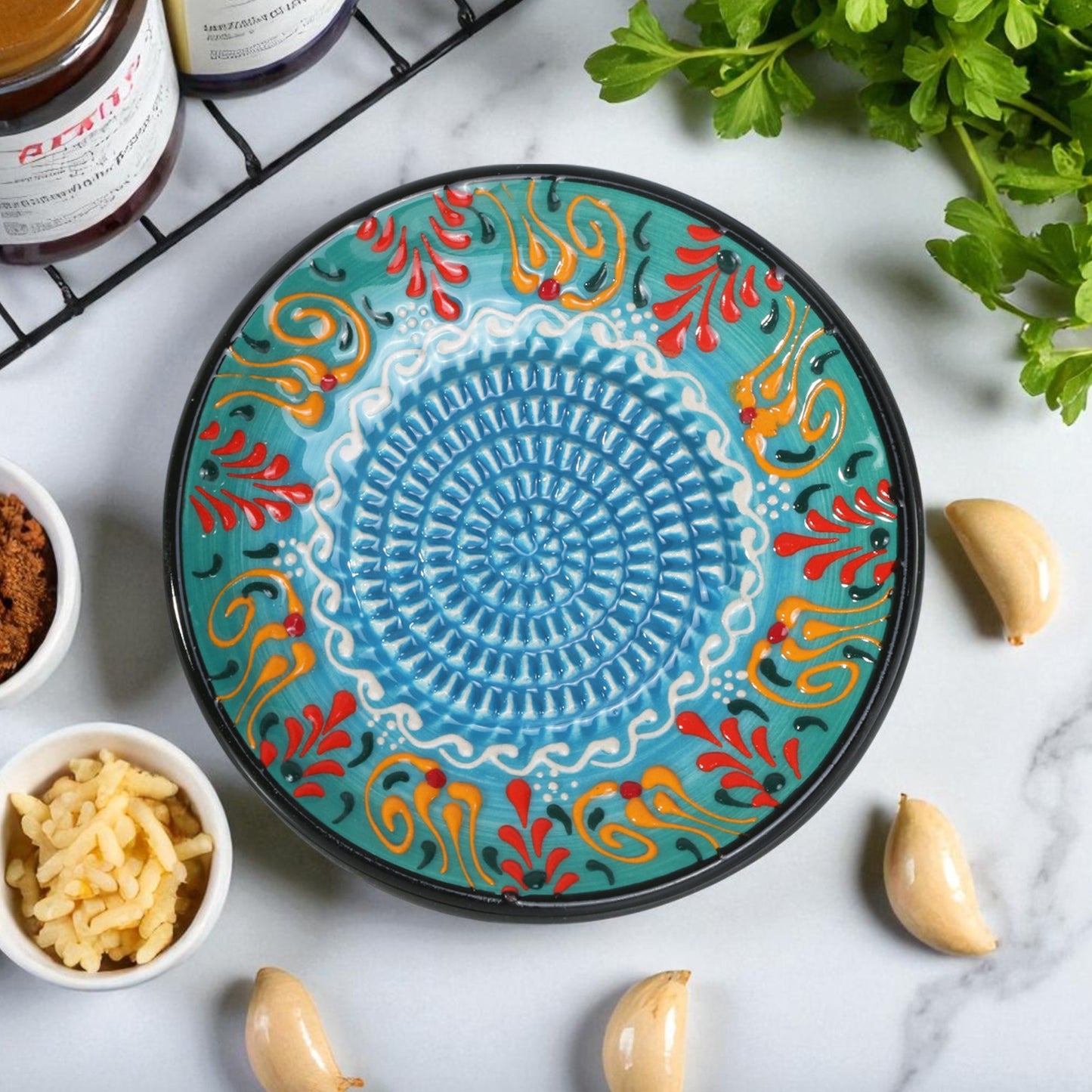 Decorative ceramic garlic grater plate with colorful patterns on a marble surface with ingredients.