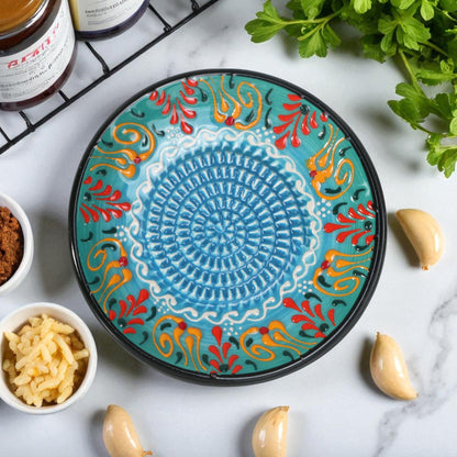 Decorative ceramic garlic grater plate with colorful patterns on a marble surface with ingredients.