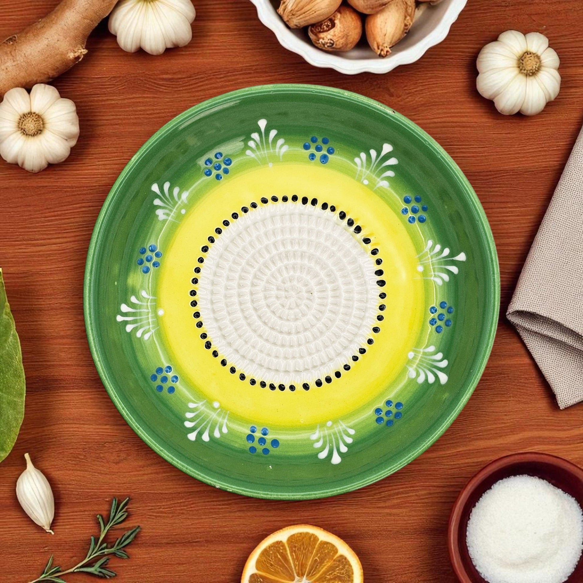 Decorative garlic grater bowl with green rim and yellow center on a wooden surface with ingredients.