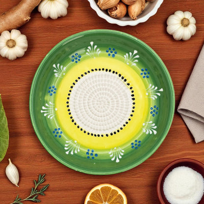 Decorative garlic grater bowl with green rim and yellow center on a wooden surface with ingredients.