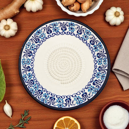 Decorative ceramic garlic grater plate with blue floral patterns on a wooden surface with pumpkins and a napkin.