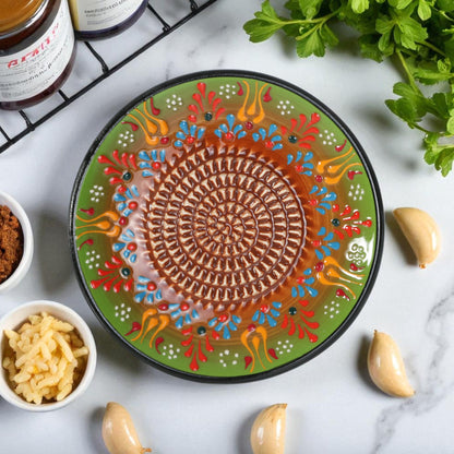 Decorative ceramic garlic grater plate with colorful patterns on a marble surface with ingredients.