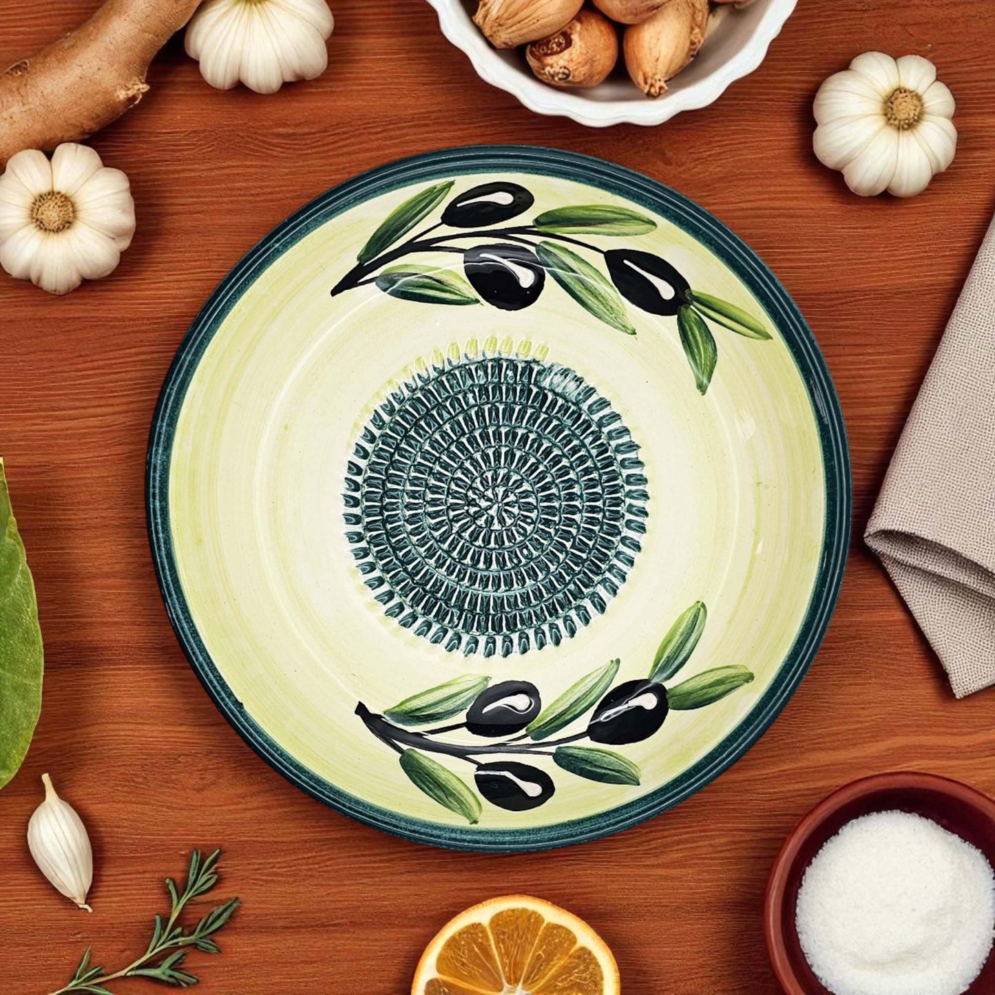 Decorative ceramic garlic grater bowl with olive design on a wooden table with ingredients.