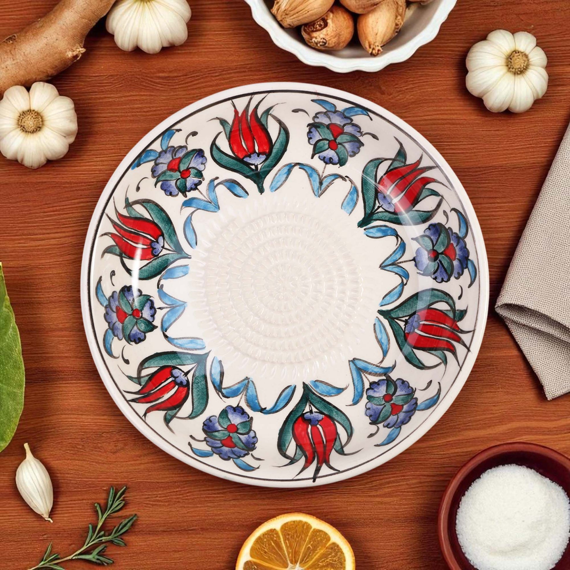 Decorative ceramic garlic grater bowl with floral patterns on a wooden table with ingredients.