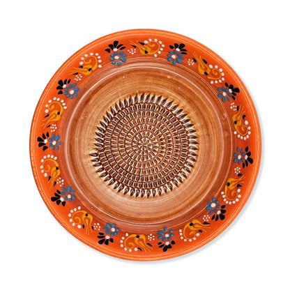 Decorative ceramic garlic grater bowl with orange rim and intricate patterns on a white background