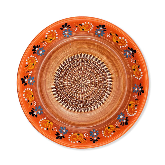 Decorative ceramic garlic grater bowl with orange rim and intricate patterns on a white background