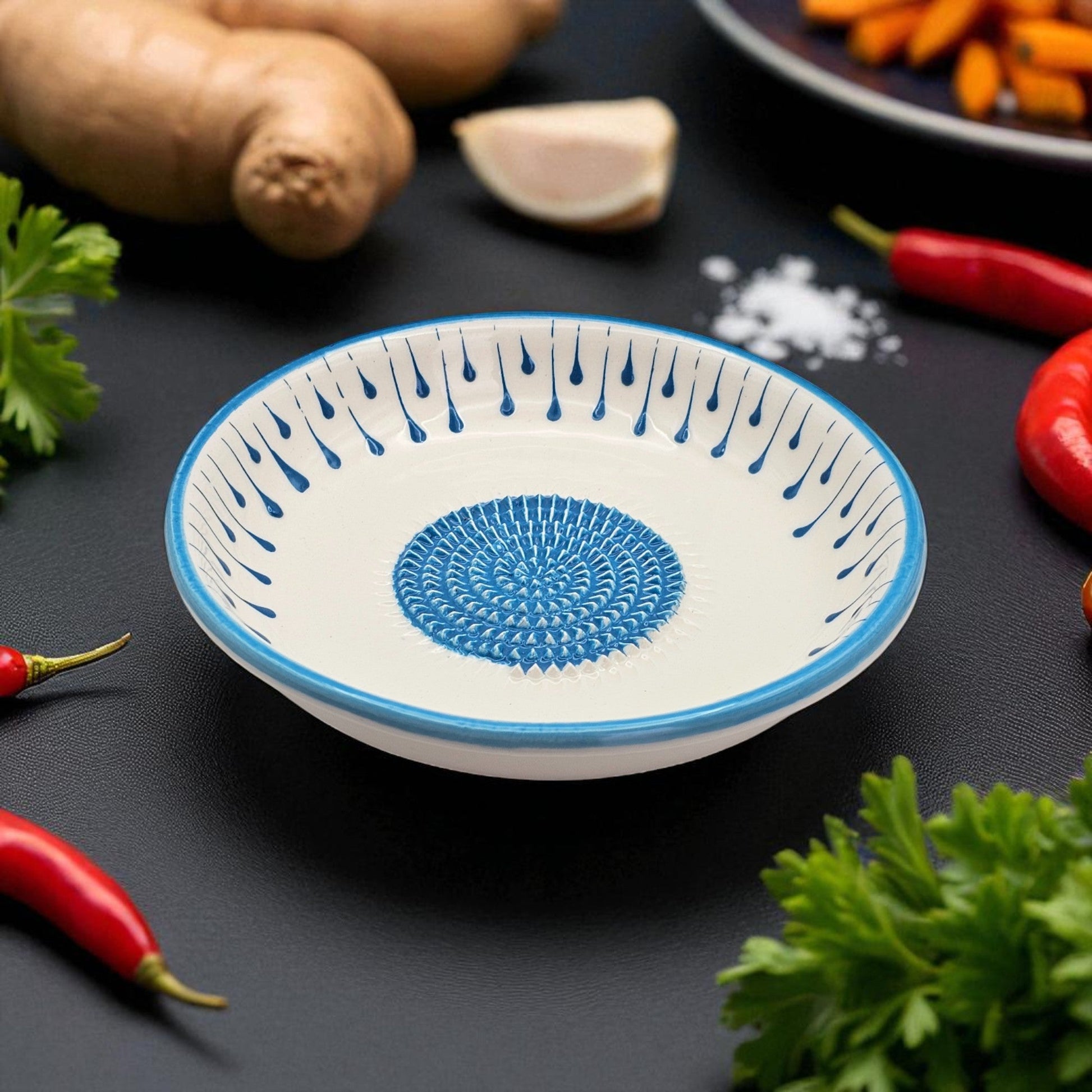 Decorative ceramic garlic grater bowl with blue patterns on a dark surface with vegetables.