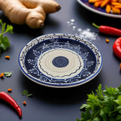 Decorative blue and white garlic grater bowl on a dark surface with spices and herbs around