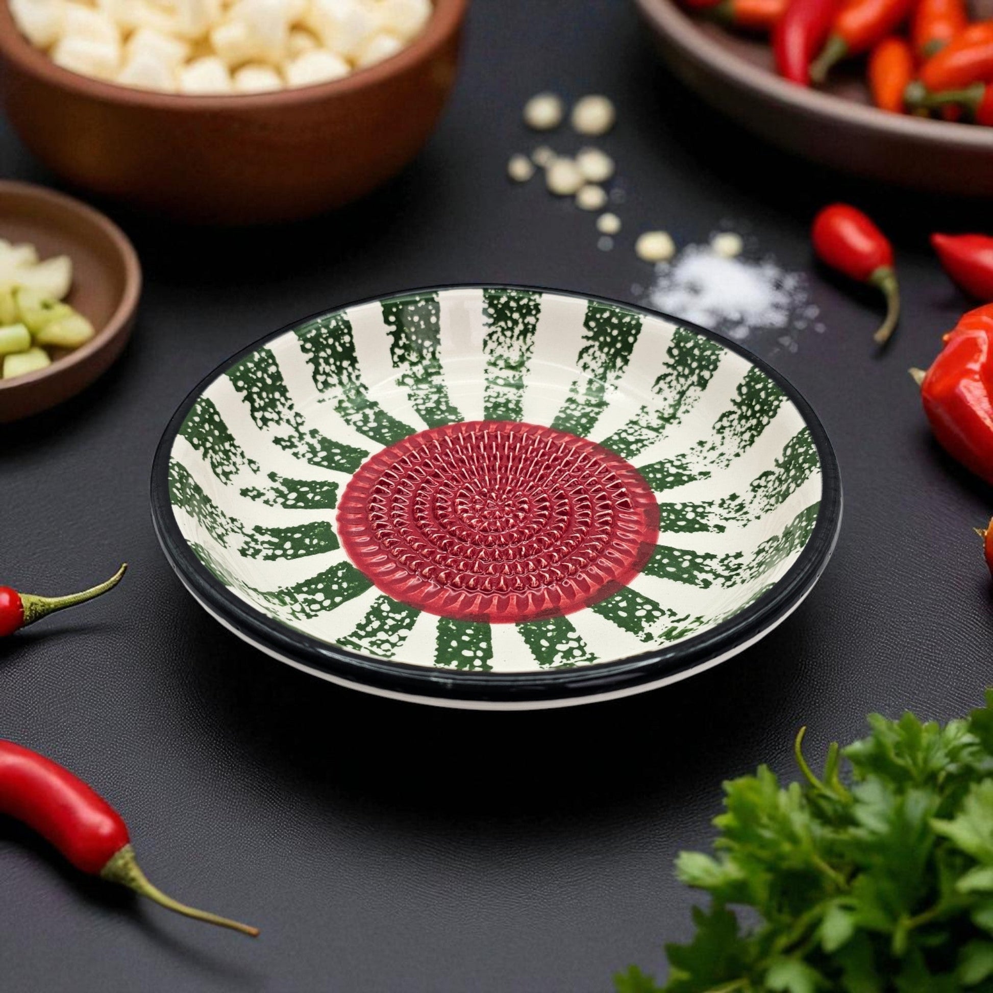 Decorative garlic grater bowl with green and red pattern on a dark surface with vegetables.