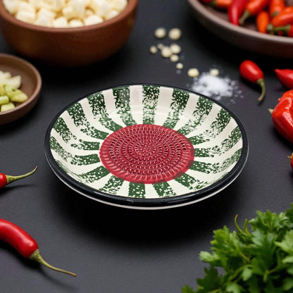 Decorative garlic grater bowl with green and red pattern on a dark surface with vegetables.