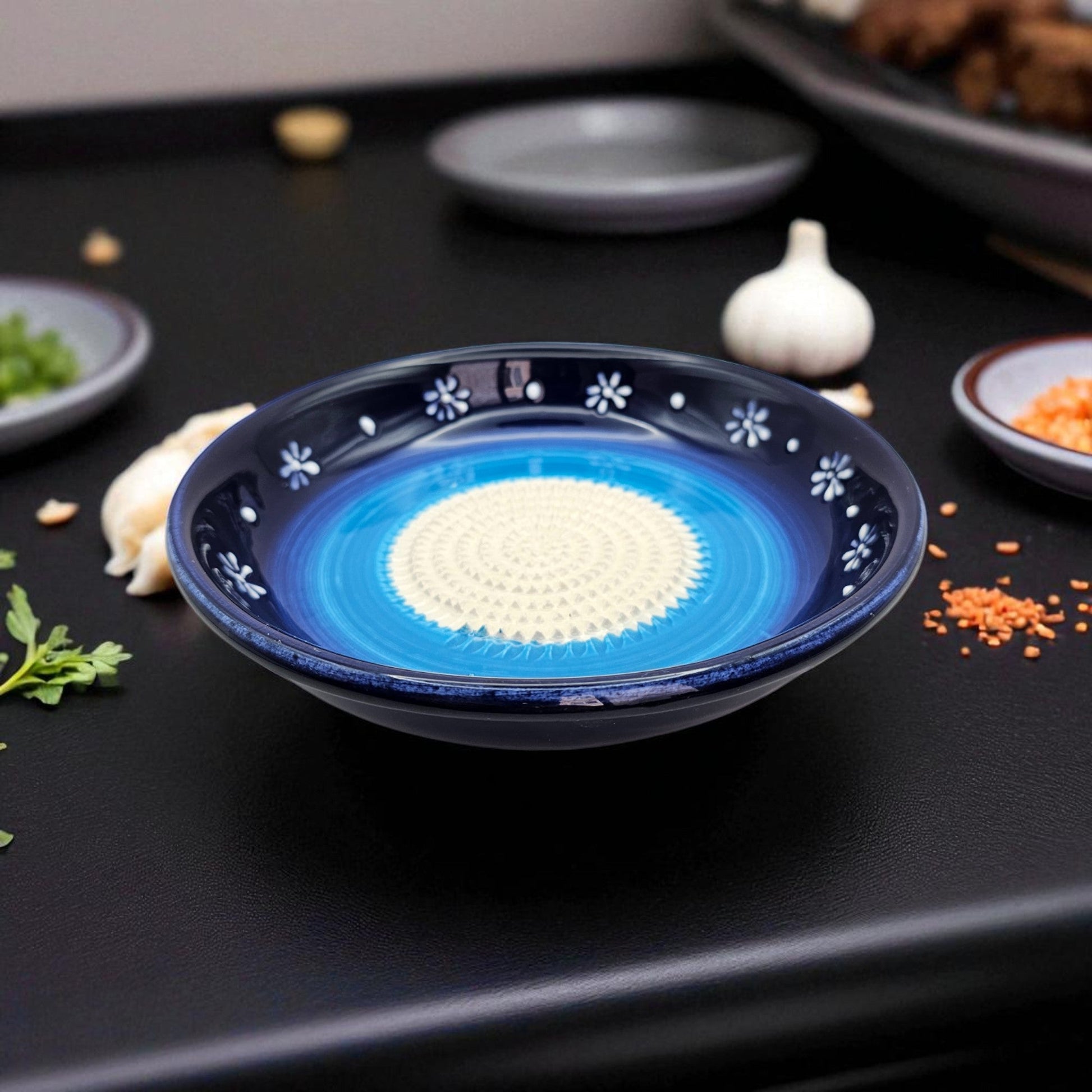 Blue ceramic garlic grater bowl with white interior on a dark surface with ingredients around