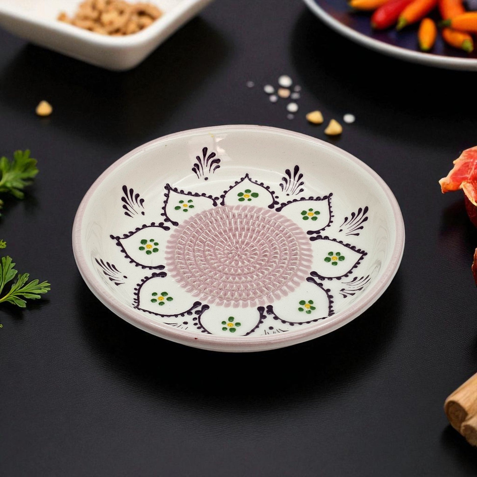 Decorative ceramic garlic grater bowl with intricate patterns on a dark surface with food items.