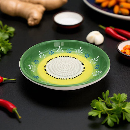 Decorative green garlic grater bowl with a yellow center on a dark surface with ingredients around