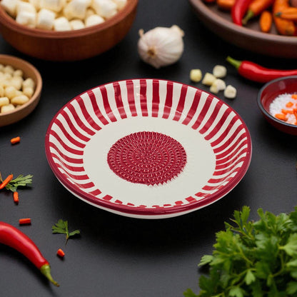 Red and white decorative garlic grater bowl on a dark surface with vegetables around