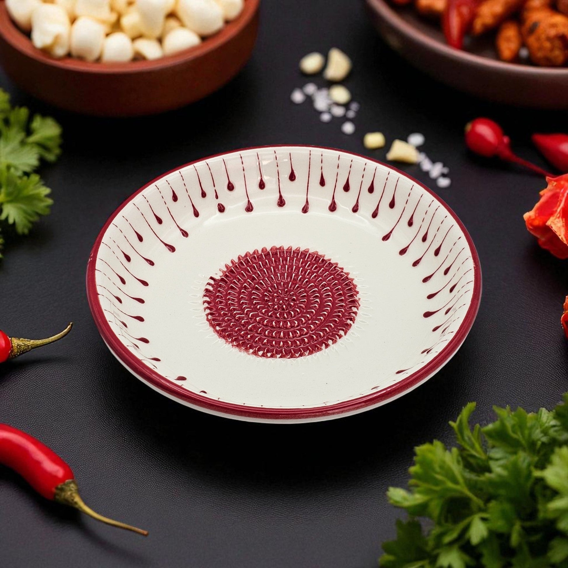 Decorative garlic grater bowl with red patterns on a dark surface with ingredients around