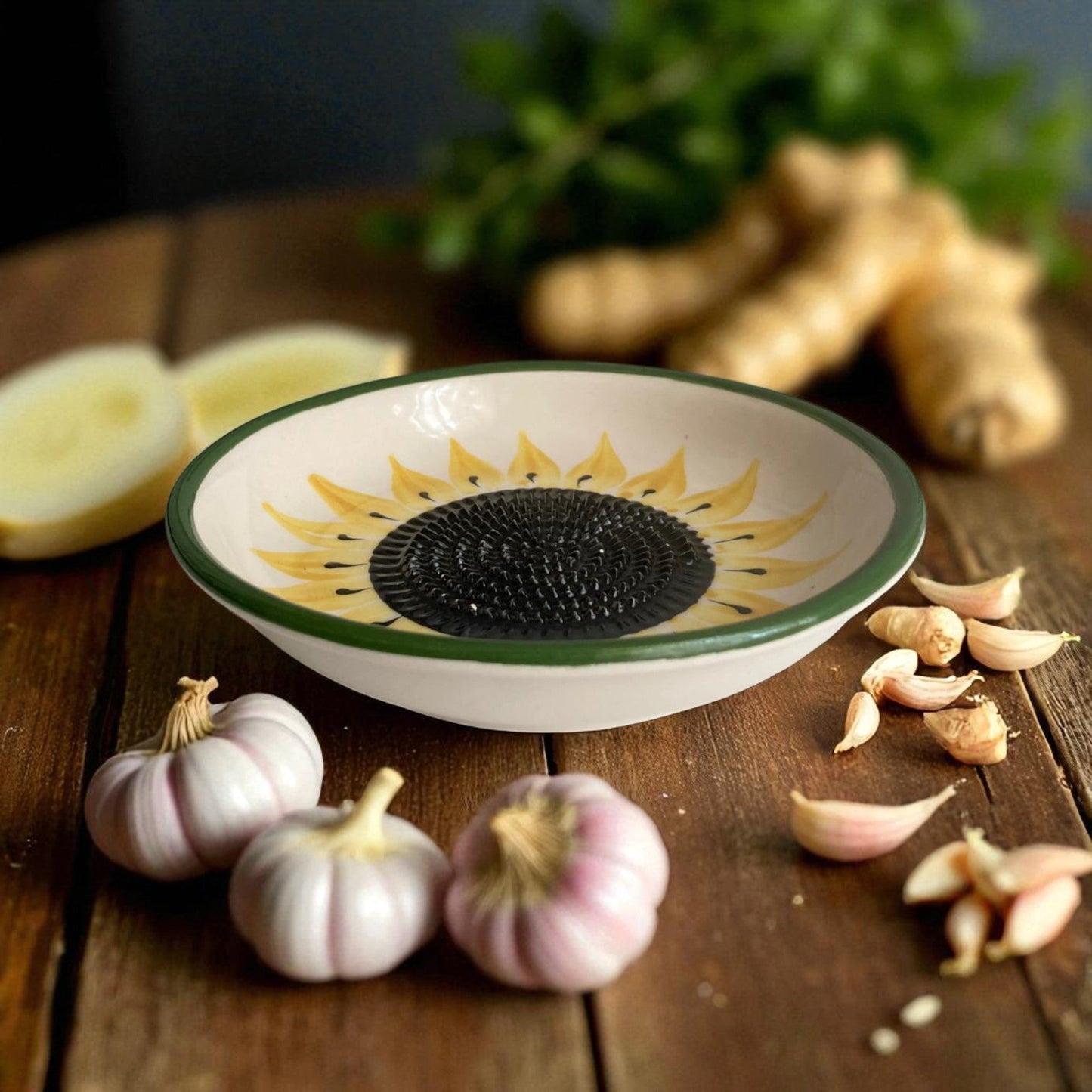 Decorative sunflower-patterned garlic grater bowl on a wooden surface with garlic and ginger.