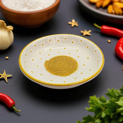 Decorative ceramic garlic grater bowl with gold center on a dark surface with ingredients