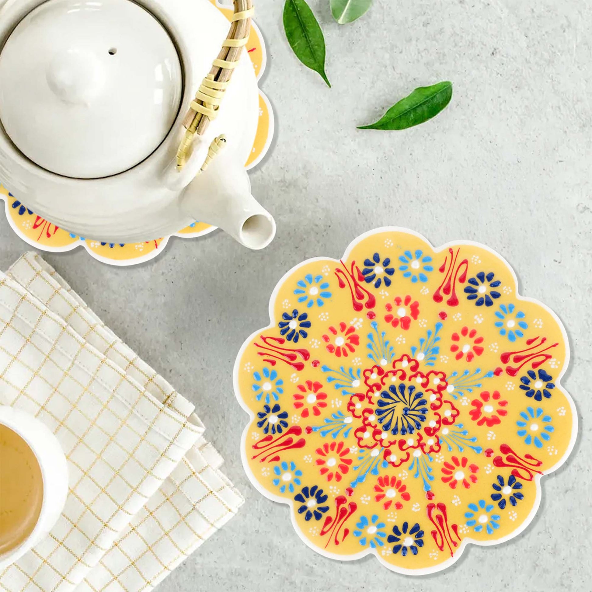 Colorful floral trivet on a gray surface with a teapot and cup.